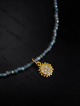 Halskette mit blauen Glasperlen, in der Mitte ist ein kleiner goldener Sonnenanhänger mit kleinen Zirkonia Steinen